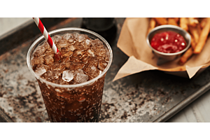 A close-up of a fizzy soda filled with Hoshizaki Cubelet chewable ice and a red and white straw, served next to an order of fries and ketchup on a metal tray