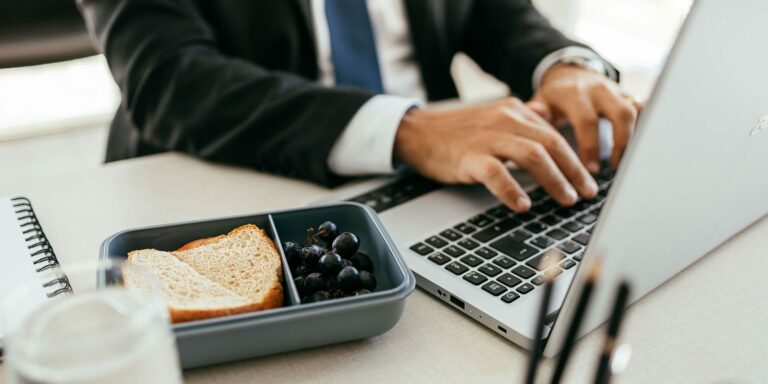 A corporate employee eating lunch while working at a laptop, representing Hoshizaki equipment used in a business office setting