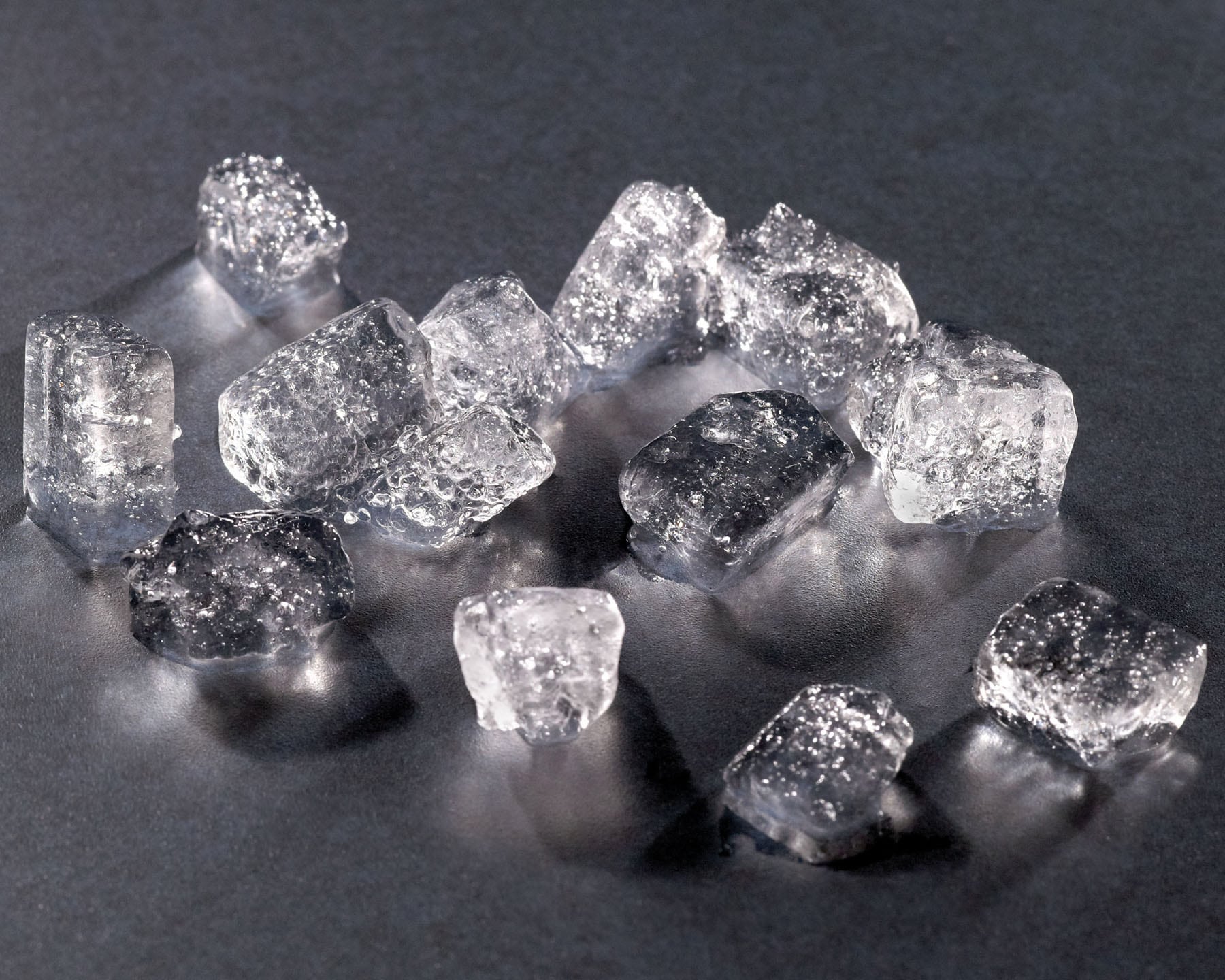 A pile of small, chewable, cylindrical Hoshizaki cubelet ice pieces with a slightly frosted appearance, resting on a reflective surface
