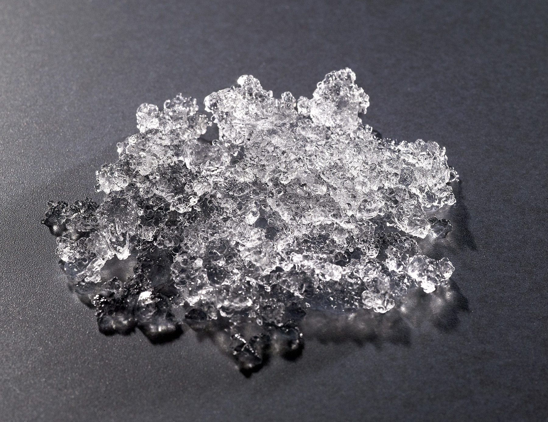 A detailed close-up shot of small, porous, and chewable Hoshizaki flaked ice gathered in a pile on a dark, textured surface
