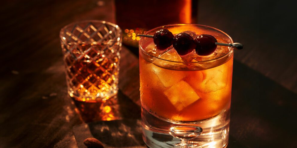 A classic cocktail garnished with three cherries and containing clear Hoshizaki gourmet ice cubes, set on a dark wooden table
