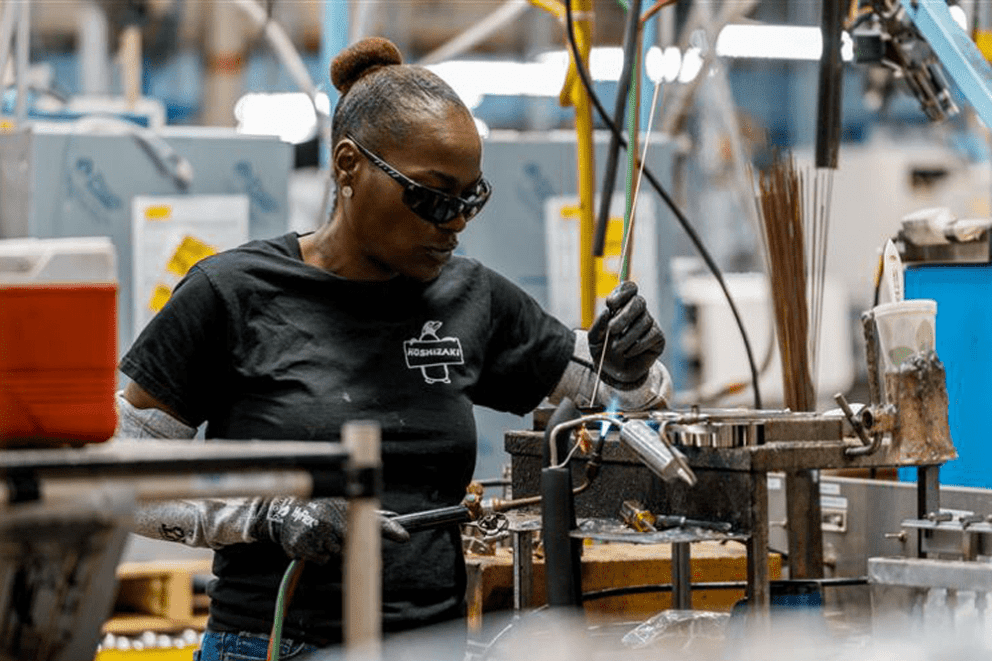 A skilled factory worker in a Hoshizaki t-shirt and safety gear uses a torch to braze a refrigeration component on the production line
