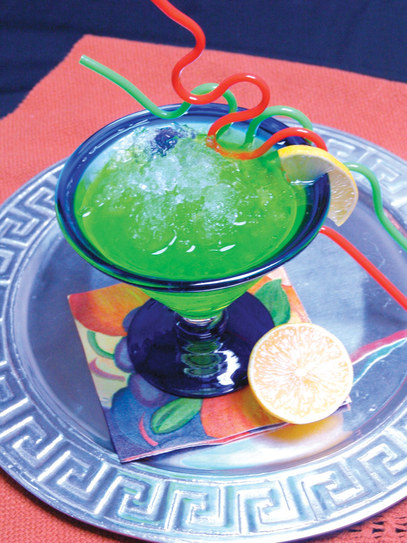 A brightly colored green beverage, likely a slushie or frozen margarita, featuring Hoshizaki flaked ice, garnished with a lemon slice and colorful straws