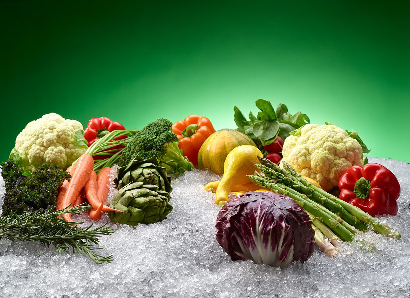 A vibrant display of colorful fresh produce, including cauliflower, peppers, and asparagus, resting on a bed of Hoshizaki flaked ice to maintain market freshness