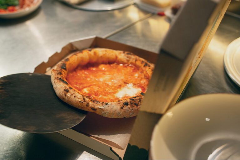 A fresh margherita pizza is being placed into a takeaway box, likely kept warm and ready for pickup using Hoshizaki heated cabinets or holding equipment