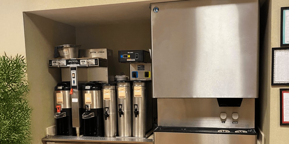A self-service beverage station featuring a stainless steel Hoshizaki ice and water dispenser positioned next to multiple coffee brewers and insulated carafes