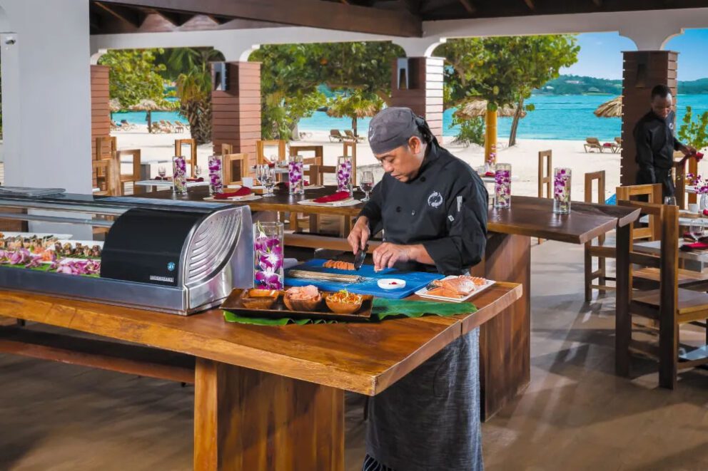 Chef cutting fish at a sushi case display, featuring Hoshizaki refrigerated equipment in an outdoor resort setting