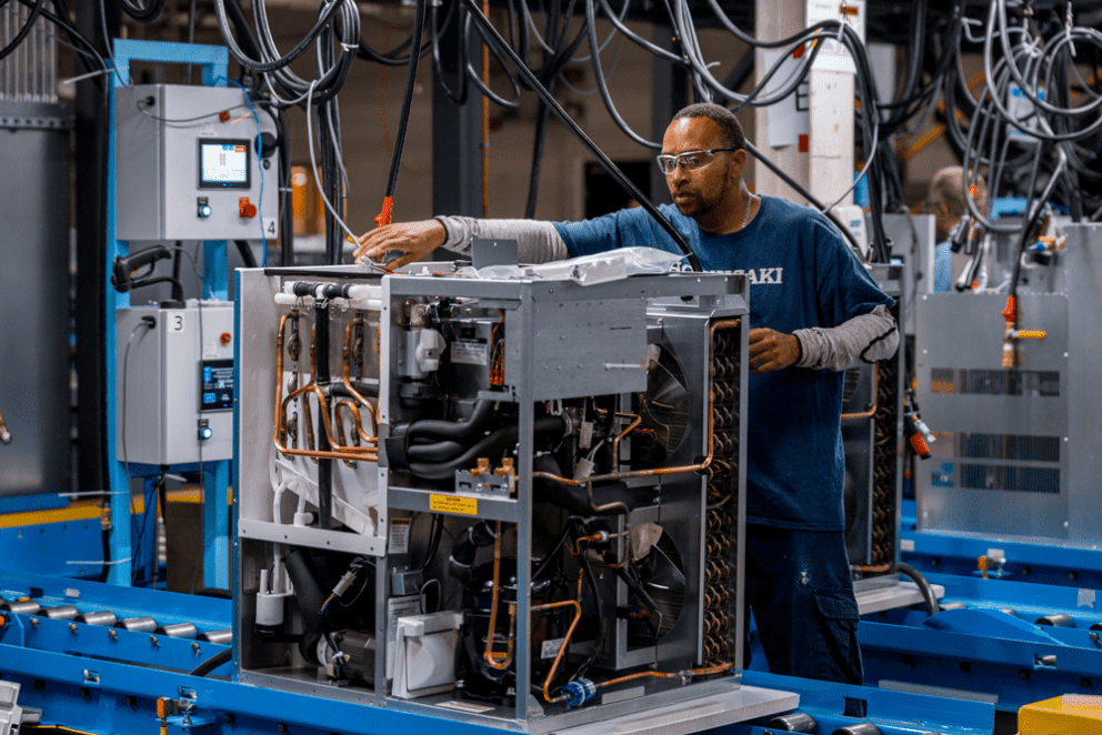 A skilled Hoshizaki technician in safety glasses is meticulously assembling a refrigeration unit on the factory's production line